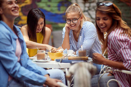 group of young adult caucasin female friends socializing in outdoor cafe, drinking coffee, smiling, laughingの写真素材