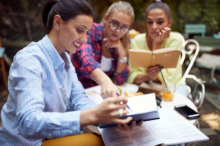 three young adult caucasian women studying together in outdoor cafe.の写真素材