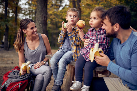 A couple and their children enjoying eating fruits in the forest on a beautiful autumn dayの写真素材