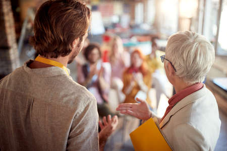 An elderly female boss is introducing her colleague who will held a presentation for employees in a...