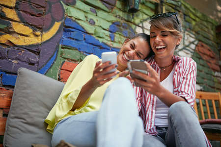 two gorgeous caucasian female friends laughing loud looking something on their cell phonesの写真素材