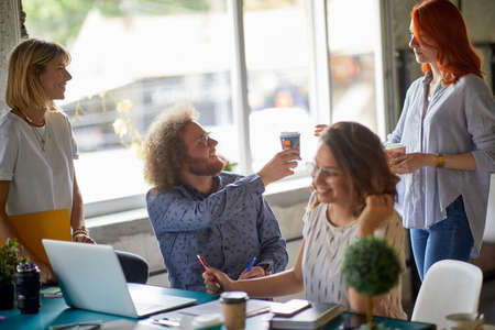 Group of young creative colleagues enjoying coffee while working in a friendly atmosphere in the...
