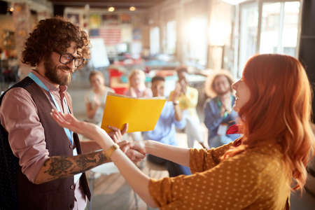 young redhead female congratulate to a caucasian business student after successful attending seminar, giving him certificate in folder. selective focus image.の写真素材