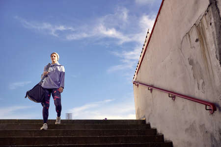 Activity girl runner holds sport bag, training on stadiumの写真素材
