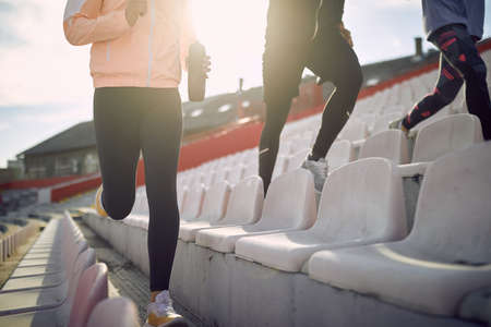 A group of young people is jogging on the grandstand while having a training on a beautiful day at the stadium. Sport, athletics, athletesの写真素材