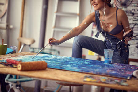 A young sexy and attractive female artist is enjoying the music while painting in a relaxed atmosphere in her studio. Art, painting, studioの写真素材