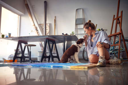 Young hot female artist playing with her dog in the studio
