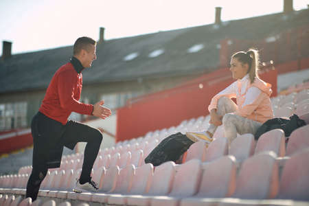caucasian personal trainer talking, explaining, with a smile and hand gesture to young adult femaleの写真素材