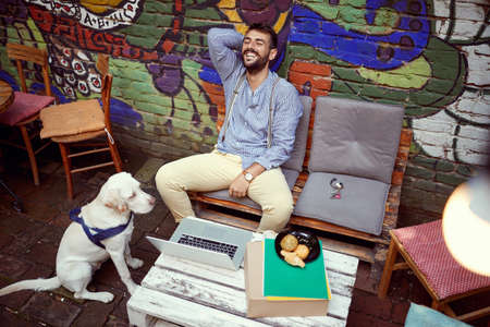 young adult beardy caucasian male having a break in outdoor cafe, laughing out loud, amused by his dog focused on a foodの写真素材