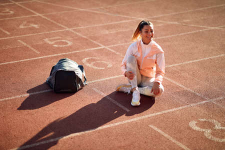 happy and satisfied looking caucasian female talking on her cell phone with headphones in her ears, hands free, sitting on the running path, smiling, laughingの写真素材