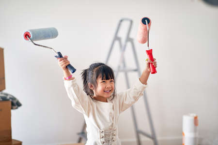 A little girl in a cheerful atmosphere is excited about painting a new home she just moved in with the family. Home, family, movingの写真素材