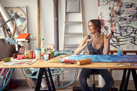 A young sexy and attractive female artist in a pleasant atmosphere in her studio finds the inspiration for painting while listening to the music. Art, painting, studioの写真素材