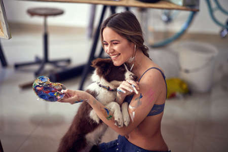 A young sexy and attractive female artist in a bra in emotional moments with her dog while taking a break from painting in a relaxed atmosphere in her studio. Art, painting, studioの写真素材