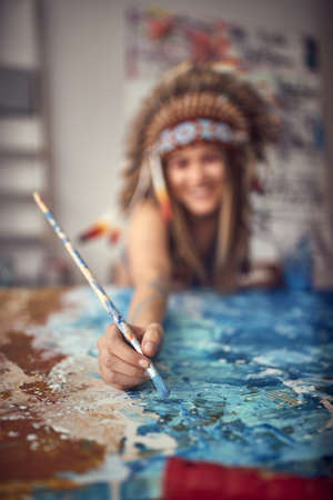 Close-up of a brush of a young sexy female artist with a war bonnet who is painting in a pleasant atmosphere in her studio. Art, painting, studioの写真素材