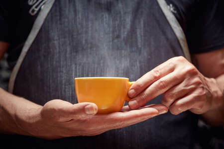 Barista holding a yellow cup of fresh dark coffeeの写真素材