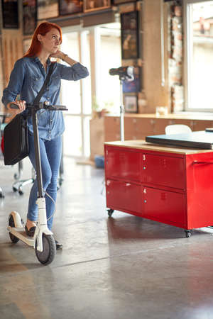 Young female employee on a scooter posing in a relaxed atmosphere in the office