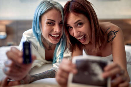 Very delighted lesbian couple showing ultrasonic image of future babyの写真素材