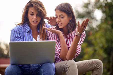 Young beautiful female friends doing some work on the laptop together while sitting outside on a beautiful weather. Friendship, together, workの写真素材
