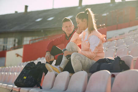 Young woman and man are chatting while sitting on the grandstand after a training on a beautiful day at the stadium. Sport, athletics, athletesの写真素材
