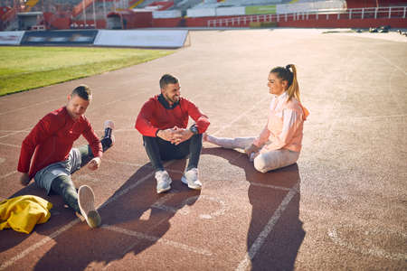 young adult caucasian beardy guy sitting on athlete track together with smiling couple to whom is talking. personal trainer conceptの写真素材