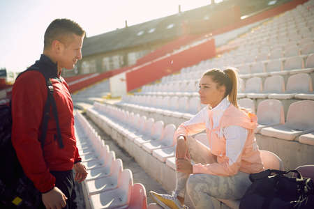 Young woman and man are chatting on the grandstand after a training on a beautiful day at the stadium. Sport, athletics, athletesの写真素材