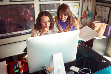 Two beautiful female colleagues are working in a pleasant atmosphere  in the office togetherの写真素材