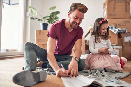 A young father with his daughter in a family atmosphere is enjoying the new home they have just moved in. Home, family, movingの写真素材