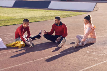 caucasian personal trainer talking, explaining with hand gesture to young adult couple, preparing for training, stretchingの写真素材