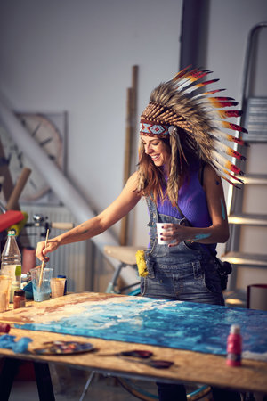 A young female artist with a war bonnet enjoys working on her new painting in a pleasant atmosphere...