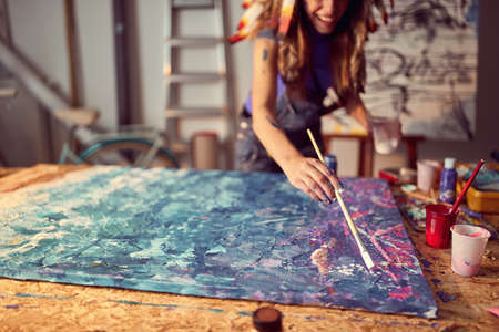 A young female artist with a war bonnet in a creative atmosphere in the studio is working on an abstract painting. Art, painting, studioの写真素材