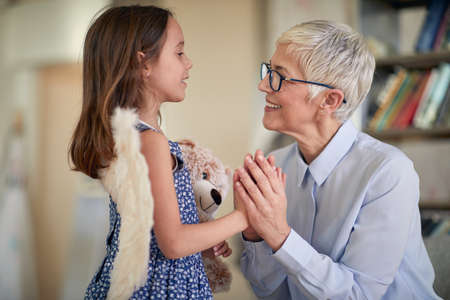 A happy grandma enjoys talk with her little granddaughter while holding her hands in a family atmosphere at home. Family, home, love, playtimeの写真素材