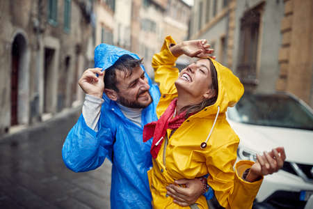 A young couple in love is in a good mood while walking the city during a rain in a cheerful atmosphere. Walk, rain, city, relationshipの写真素材