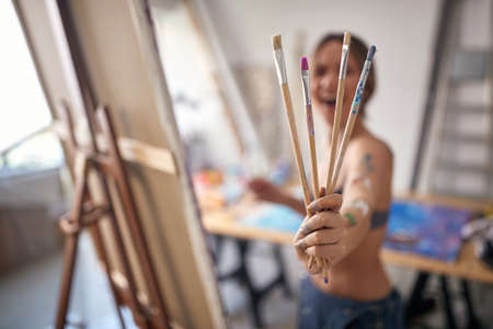 Close-up of a young sexy and attractive female artist in a bra holding bunch of brushes and posing for a photo in a relaxed atmosphere in her studio. Art, painting, studioの写真素材
