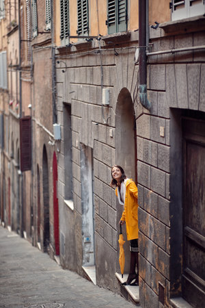 A young girl in a yellow raincoat is standing in the building entrance and checking if it is raining. Walk, rain, cityの写真素材