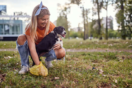 A young girl on a beautiful day in the park is cleaning up after her dog. Friendship, walk, petsの写真素材
