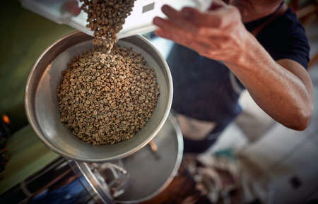 A man is pouring fragrant and aromatic coffee beans into the grinder. Coffee, beverage, producingの写真素材