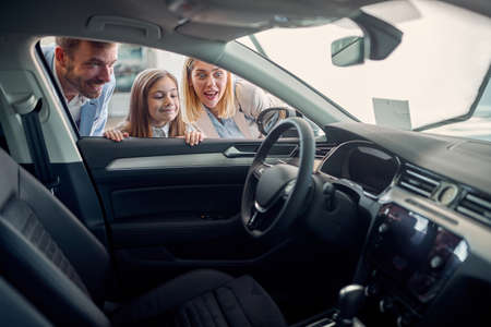 Man and woman with daughter buying new car at dealership saloon