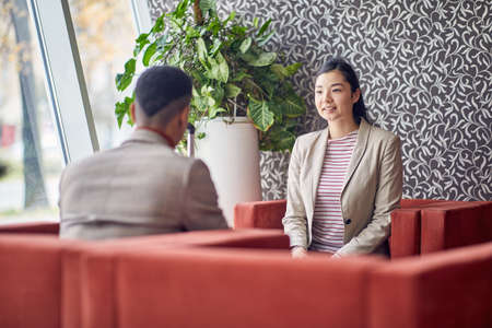 Two young business people are sitting and chatting in a relaxed atmosphere in the hotel lobby during a business trip. Business, people, hotel, tripの写真素材