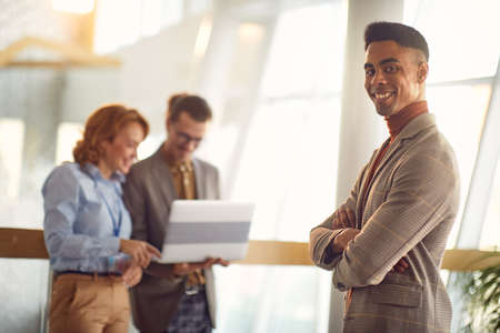 A young businessman is standing in the hallway with his colleagues and posing for a photo in a relaxed atmosphere. Business, people, companyの写真素材