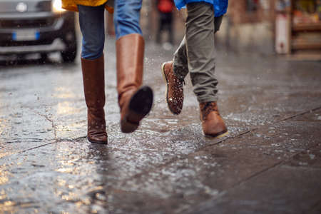 Close-up of a young couple and their legs how walking on the rain in the city in a hurry manner....