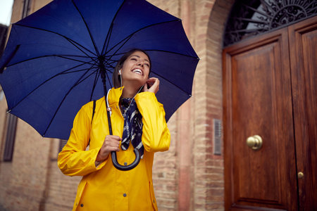 A young cheerful woman is listening to the music while walking the city in a relaxed atmosphere on a rainy day. Walk, rain, cityの写真素材