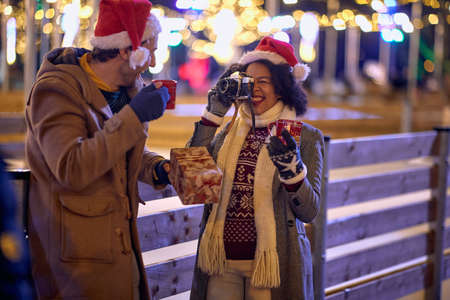 Woman taking a photo smiling boyfriend at christmas festival on a snowy weatherの写真素材