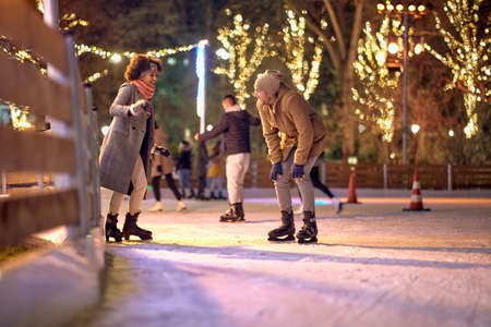 A young couple in love has a good time while skating at ice-skating rink during christmas holidays on a beautiful night in the city. Christmas, New Year, holiday, loveの写真素材