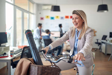 A young female employee posing for a photo while riding a bike in a relaxed atmosphere during a break in the office. Employees, job, officeの写真素材