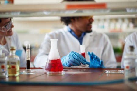 Young colleagues in a protective gear discuss while work with colorful chemicals in a relaxed atmosphere in the university laboratory. Science, chemistry, lab, peopleの写真素材