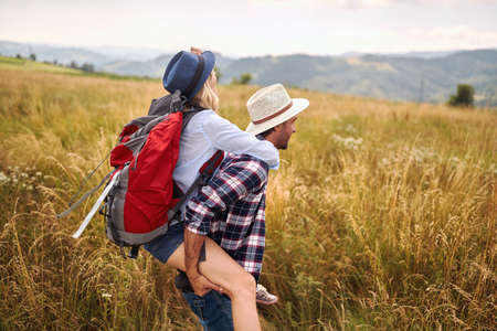 A young happy couple in love is having fun while enjoys walking a meadow on a beautiful sunny day. Hiking, nature, relationship, togetherの写真素材