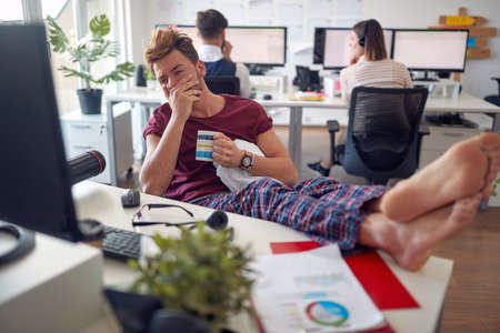 A young male employee is working at the desk while sitting in a relaxed manner in a pleasant atmosphere in the office. Employees, job, officeの写真素材