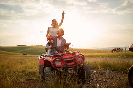 Young newlyweds are enjoying quad ride on a beautiful sunny day in the nature. Riding, wedding,...