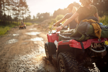 Young girls ride quads on a muddy road on a beautiful sunny day in the nature. Riding, nature, friendship, togetherの写真素材