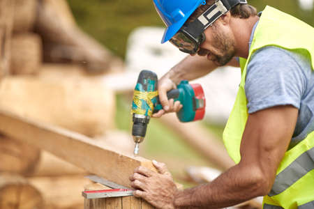 Close-up of handsome male builder working with tools at the construction site in the forest on a...